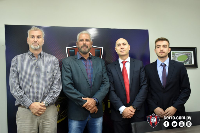 Quatro homens posando em frente a um painel do Cerro Porteño (CP), com o site "cerro.com.py" e ícones de redes sociais visíveis.