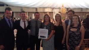 Sete pessoas em pé posando para a foto, a pessoa do meio segurando um Certificado da Rotary Club.