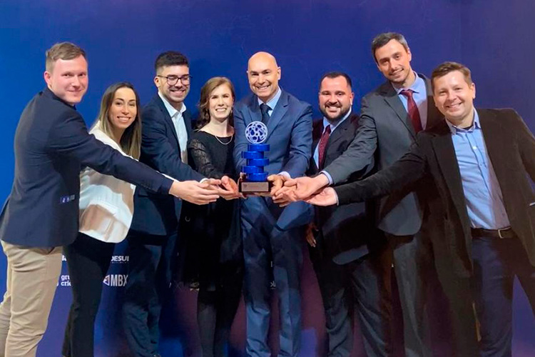 Um grupo de oito pessoas em trajes formais, sorrindo e segurando um troféu azul juntos.
