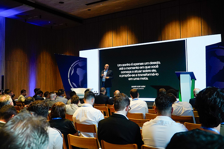 Um palestrante apresenta-se a uma plateia em uma conferência. A tela exibe uma citação motivacional.