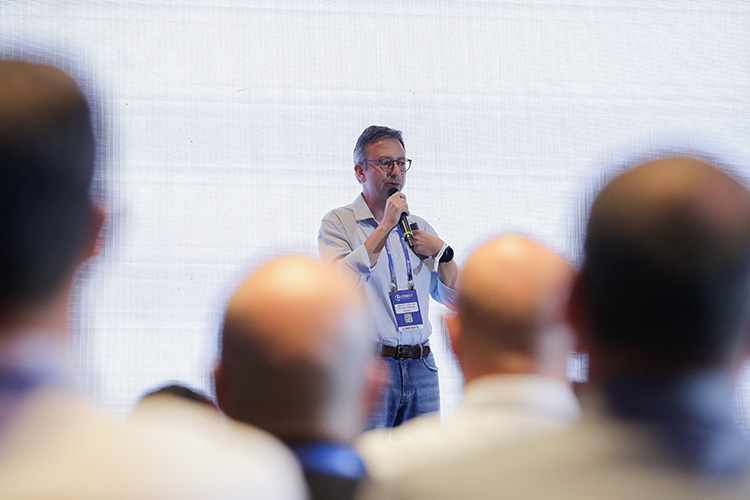 Um palestrante em uma conferência, usando um microfone, fala para um público desfocado.