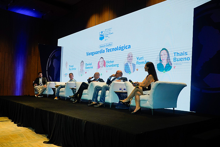 Painel de discussão com seis participantes sentados em sofás brancos diante de uma tela exibindo seus nomes e fotos. O painel discute "Vanguarda Tecnológica".