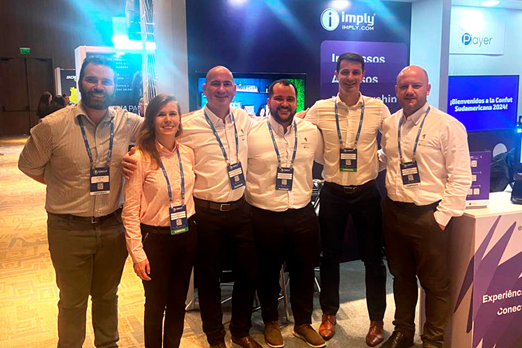 Grupo de seis colegas sorrindo, usando crachás de conferência, em um evento.