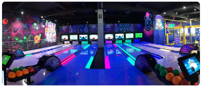 Vista de 8 pistas de boliche com repositores de bolas e com canaletas acesas nas cores verde e rosa.