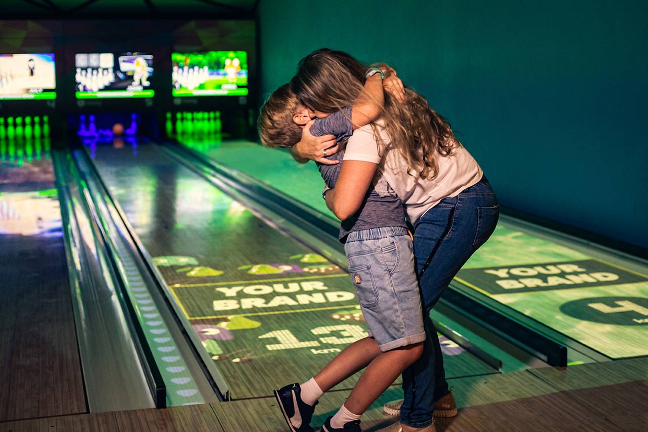 mãe e filho se abraçando em uma pista de boliche