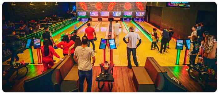 Vista de cima no início de uma pista de boliche, com várias pessoas jogando.