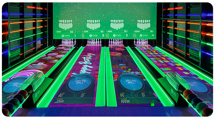 Vista completa de uma pista de boliche, com vários LEDs nas paredes, canaletas acesas em verde, repositores de bolas de boliche e com desenhos nas pistas.