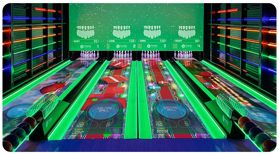 Vista completa de uma pista de boliche, com vários LEDs nas paredes, canaletas acesas em verde, repositores de bolas de boliche e com desenhos nas pistas.