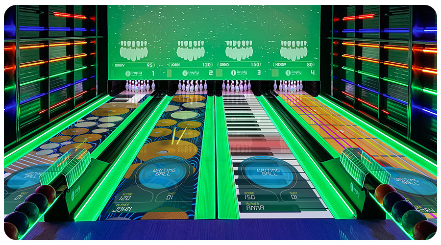 Vista completa de uma pista de boliche, com vários LEDs nas paredes, canaletas acesas em verde, repositores de bolas de boliche e com desenhos nas pistas.